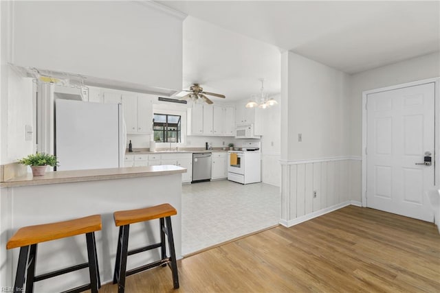 kitchen featuring white appliances, light countertops, a breakfast bar area, a chandelier, and light wood finished floors