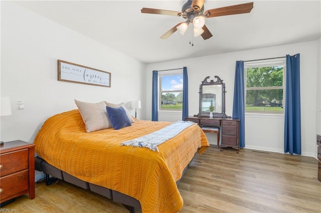 bedroom featuring multiple windows, wood finished floors, baseboards, and ceiling fan