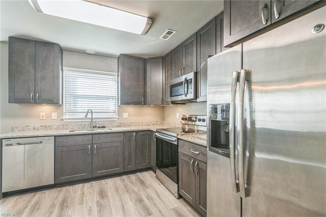 kitchen with stainless steel appliances, a sink, light stone counters, and light wood-style floors