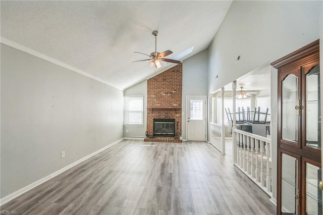 unfurnished living room featuring a ceiling fan, a fireplace, wood finished floors, a textured ceiling, and baseboards