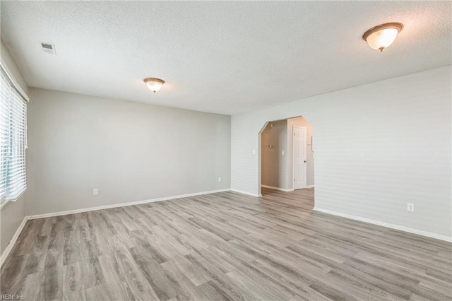 empty room featuring a textured ceiling, arched walkways, light wood-type flooring, and baseboards
