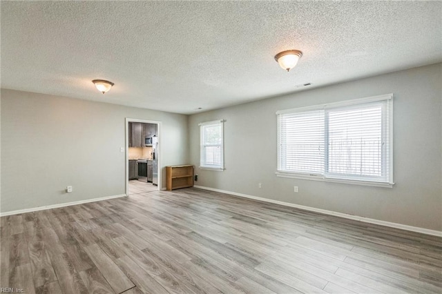unfurnished living room with light wood-style floors, a textured ceiling, and baseboards