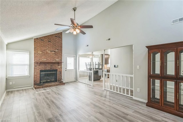 unfurnished living room with a ceiling fan, lofted ceiling, wood finished floors, a brick fireplace, and a textured ceiling