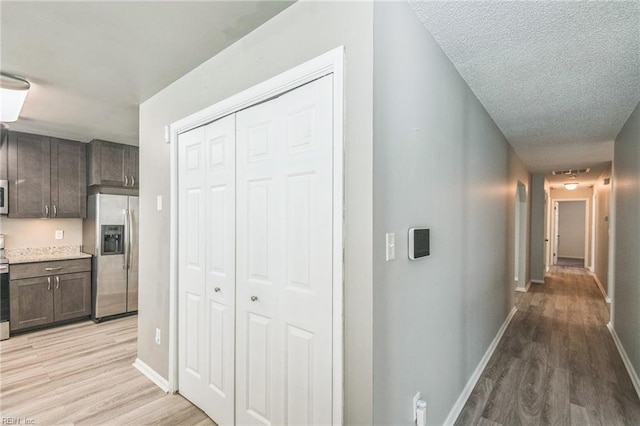 corridor with light wood-style floors, baseboards, and a textured ceiling