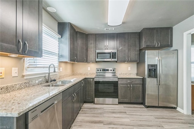 kitchen featuring stainless steel appliances, a sink, plenty of natural light, and light wood-style floors