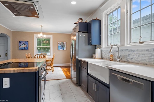 kitchen featuring butcher block counters, stainless steel appliances, crown molding, decorative backsplash, and a chandelier