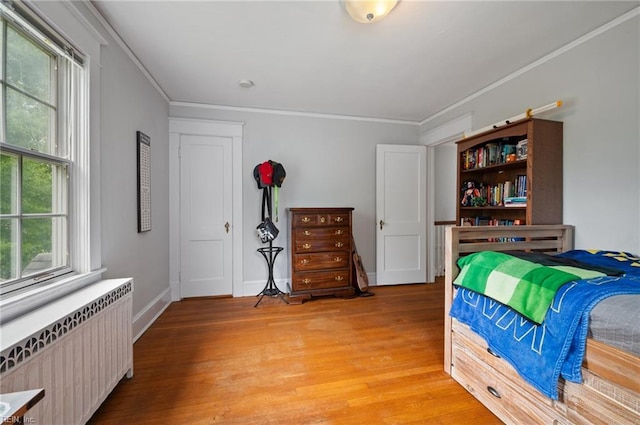 bedroom featuring radiator heating unit, light wood finished floors, crown molding, and baseboards