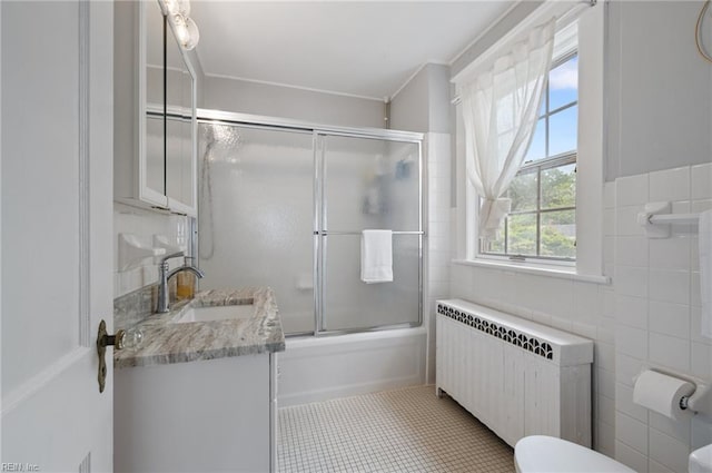 bathroom with radiator heating unit, tile walls, toilet, vanity, and tile patterned flooring