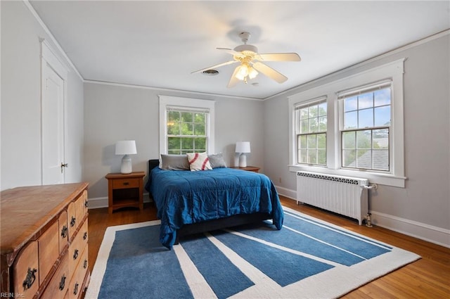 bedroom featuring radiator, multiple windows, wood finished floors, baseboards, and ornamental molding