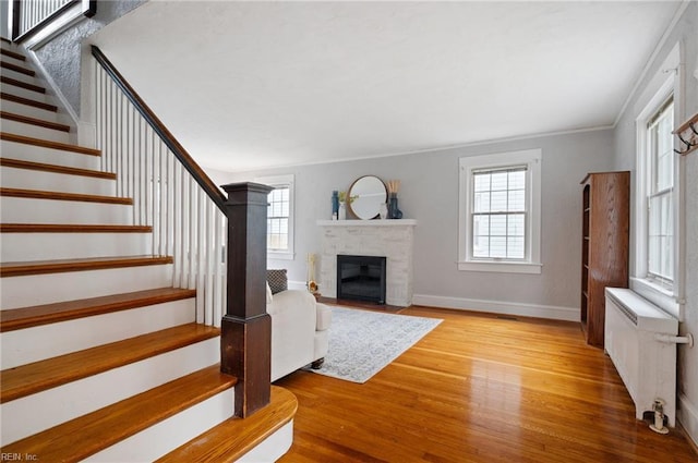unfurnished living room with radiator, stairway, wood finished floors, a fireplace with flush hearth, and baseboards