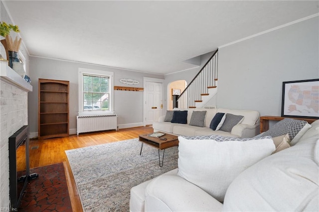 living room with radiator, a brick fireplace, wood finished floors, stairway, and ornamental molding
