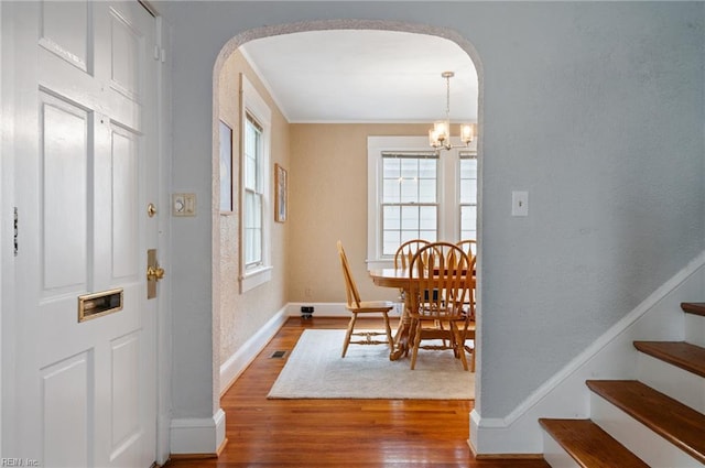foyer featuring arched walkways, wood finished floors, baseboards, and a chandelier