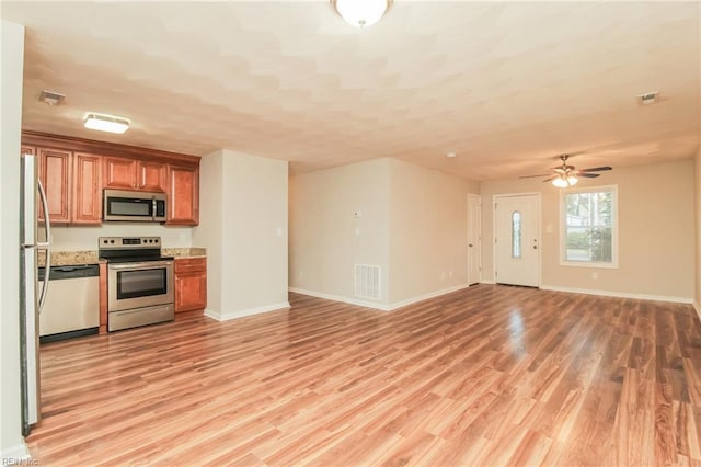 kitchen with stainless steel appliances, brown cabinetry, light wood finished floors, baseboards, and open floor plan