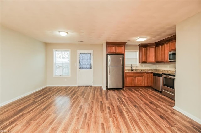 kitchen featuring stainless steel appliances, a sink, wood finished floors, and brown cabinetry