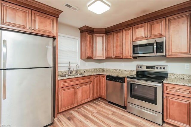 kitchen with stainless steel appliances, a sink, light wood finished floors, and brown cabinetry