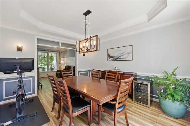 dining area with ornamental molding, light wood-style flooring, a tray ceiling, and a chandelier