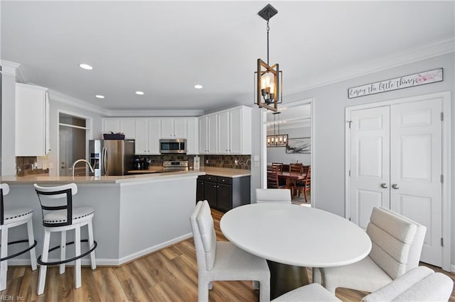 kitchen with appliances with stainless steel finishes, a chandelier, white cabinetry, light wood finished floors, and ornamental molding