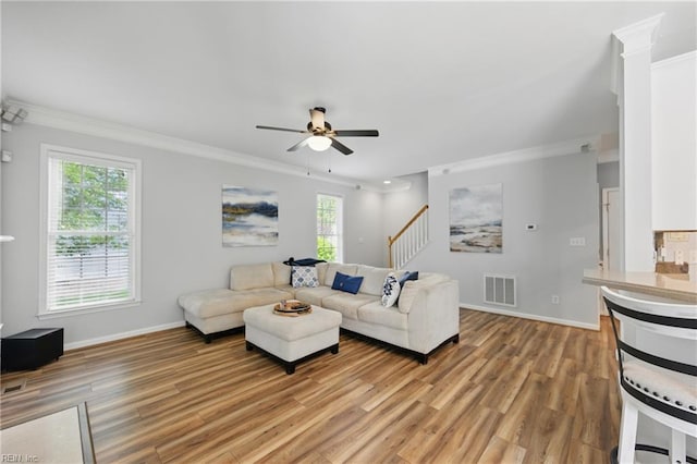 living room with crown molding, light wood-style flooring, a ceiling fan, baseboards, and stairs