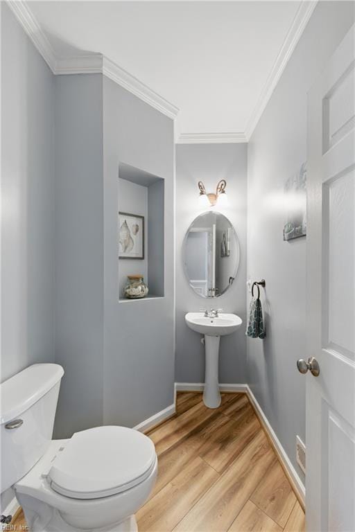 half bath with toilet, ornamental molding, wood finished floors, baseboards, and a sink