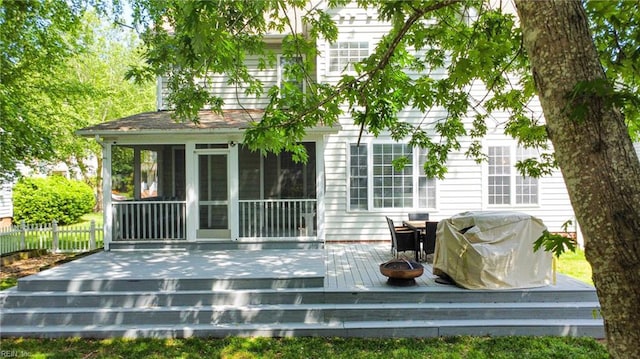 rear view of property with a wooden deck, a sunroom, a fire pit, and fence