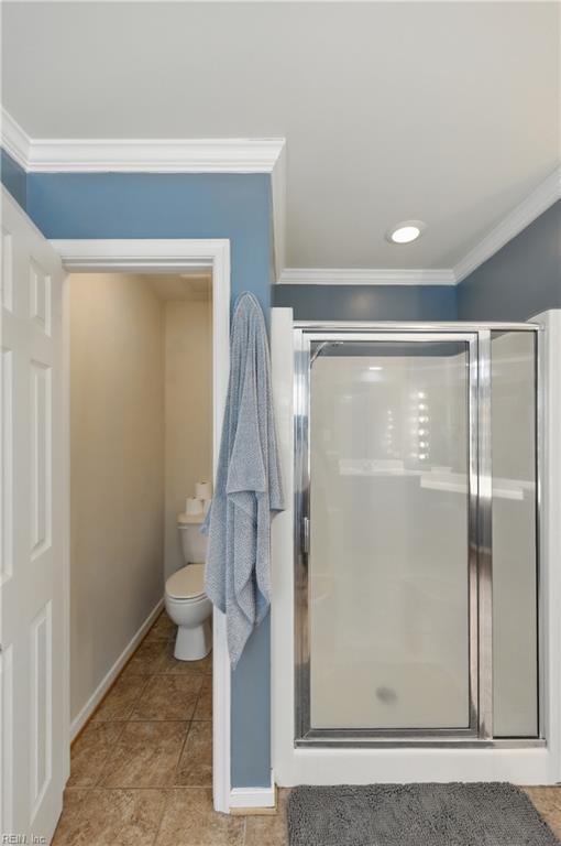 bathroom featuring ornamental molding, a shower stall, toilet, and baseboards