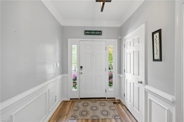 foyer with light wood-style flooring, ornamental molding, and a wainscoted wall