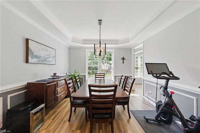 dining room featuring a raised ceiling, light wood-type flooring, wainscoting, and crown molding