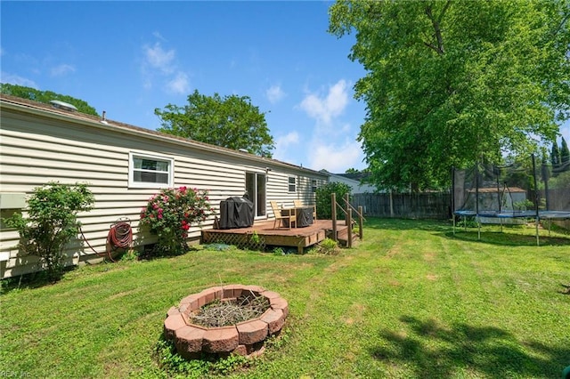 view of yard with a trampoline, a deck, and an outdoor fire pit