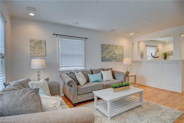 living area featuring wood finished floors, a textured ceiling, decorative columns, recessed lighting, and wainscoting