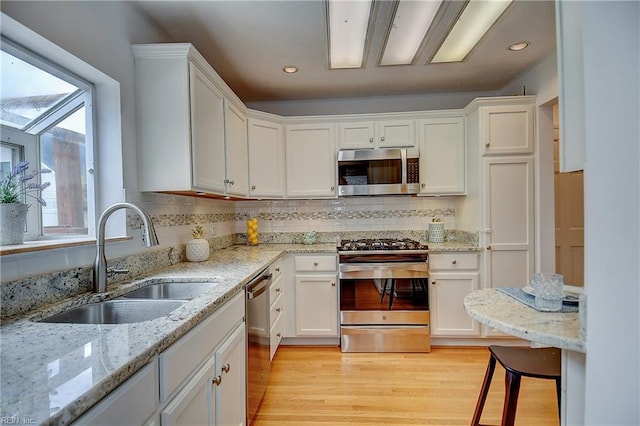 kitchen with appliances with stainless steel finishes, a sink, white cabinets, tasteful backsplash, and light wood-type flooring