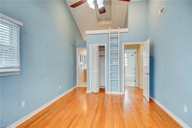 unfurnished bedroom featuring a high ceiling, wood-type flooring, a closet, baseboards, and a ceiling fan
