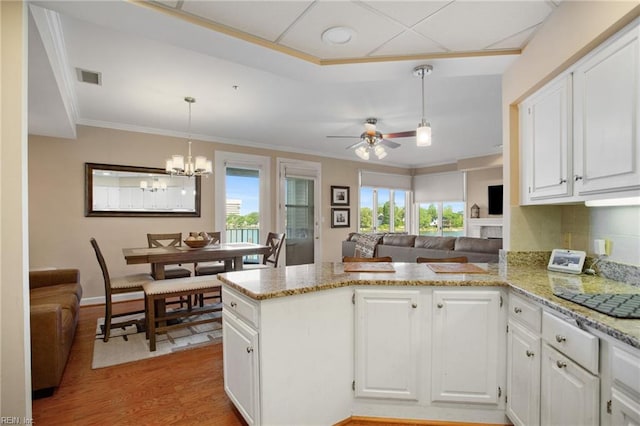 kitchen with healthy amount of natural light, a peninsula, white cabinetry, light wood-type flooring, and crown molding