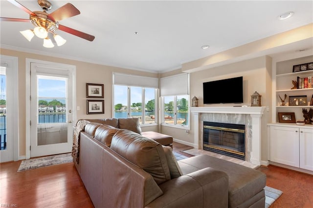 living room featuring plenty of natural light, crown molding, light wood-type flooring, a fireplace, and recessed lighting