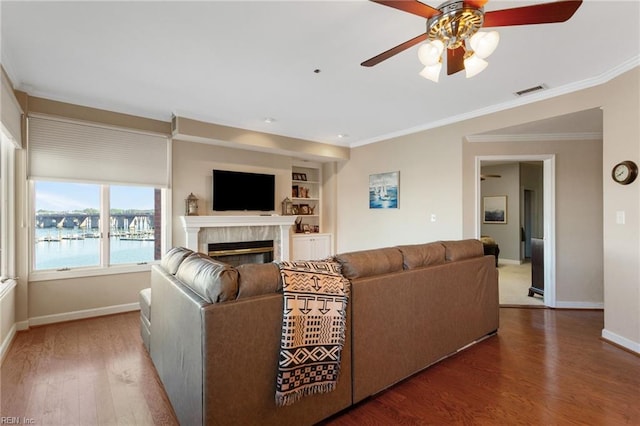 living area featuring a ceiling fan, a glass covered fireplace, crown molding, baseboards, and wood finished floors