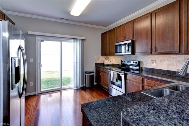 kitchen featuring stainless steel appliances, a sink, dark wood-type flooring, healthy amount of natural light, and ornamental molding