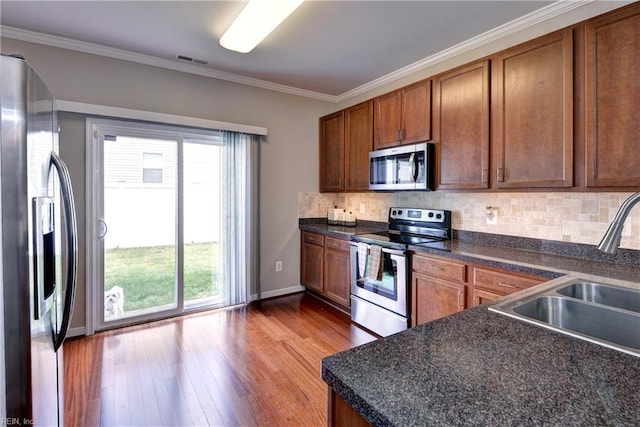 kitchen featuring appliances with stainless steel finishes, a sink, wood finished floors, dark countertops, and decorative backsplash