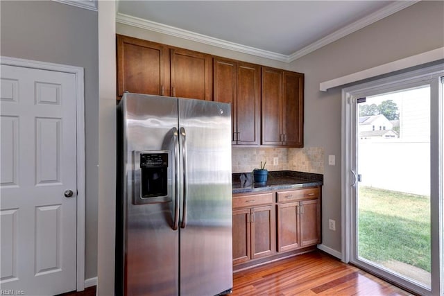 kitchen featuring stainless steel fridge with ice dispenser, backsplash, ornamental molding, light wood-type flooring, and dark stone counters