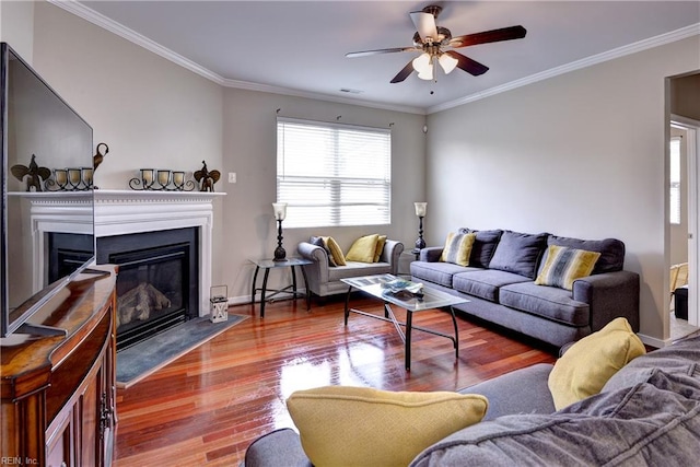living room with a ceiling fan, a glass covered fireplace, wood finished floors, crown molding, and baseboards