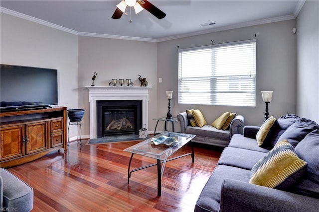 living area with ceiling fan, wood finished floors, ornamental molding, a fireplace with flush hearth, and baseboards