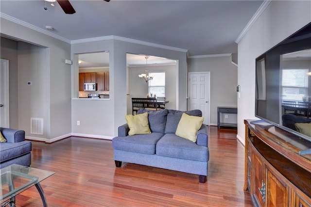 living room featuring wood finished floors, a chandelier, a ceiling fan, baseboards, and ornamental molding