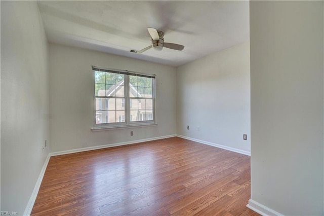 empty room with wood finished floors, a ceiling fan, and baseboards