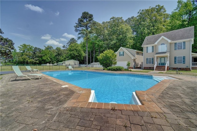 view of swimming pool featuring fence, view of scattered trees, a patio, and an outbuilding