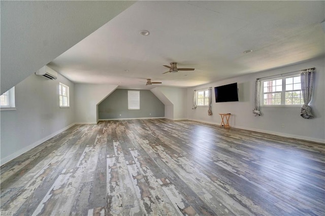additional living space with an AC wall unit, wood finished floors, healthy amount of natural light, and a ceiling fan