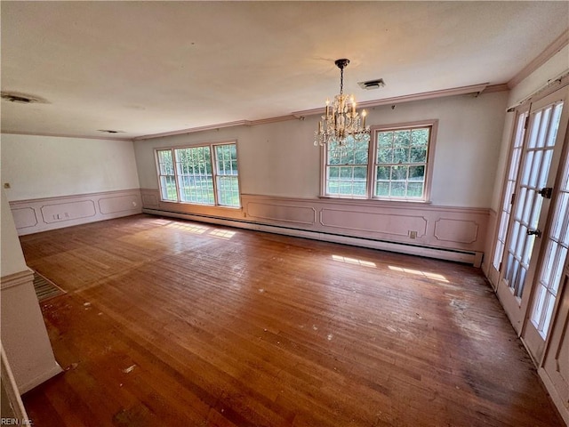 unfurnished dining area with a chandelier, ornamental molding, wood finished floors, a wainscoted wall, and a baseboard heating unit
