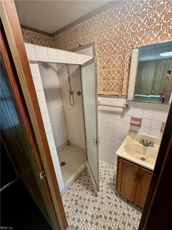 bathroom with wallpapered walls, a stall shower, a wainscoted wall, vanity, and tile walls