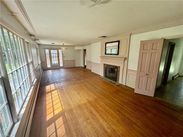 unfurnished living room featuring a chandelier, wood finished floors, a baseboard radiator, wainscoting, and a fireplace