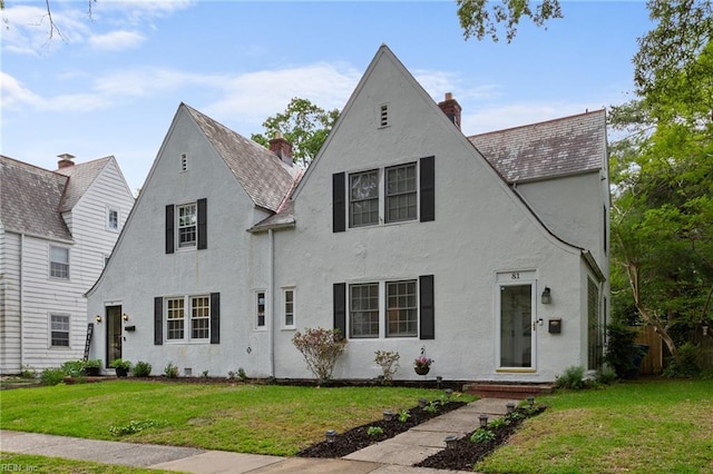 view of front facade featuring stucco siding, a front yard, and a chimney