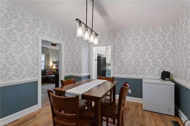 dining room featuring wallpapered walls, ornamental molding, and light wood finished floors