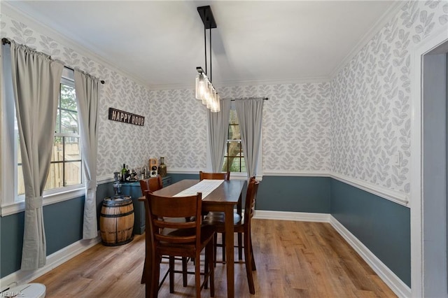 dining area with wallpapered walls, wood finished floors, baseboards, crown molding, and wainscoting