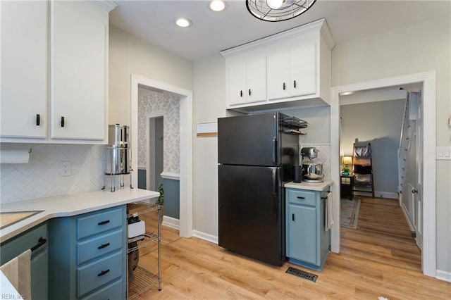 kitchen with freestanding refrigerator, blue cabinets, white cabinetry, backsplash, and light countertops